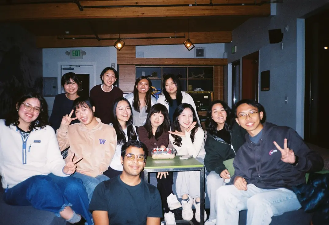 A group of friends gathered around a table, smiling and making peace signs