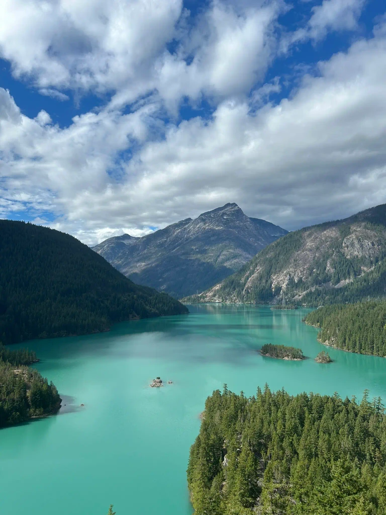 A turquoise lake between forested mountains under a cloudy sky